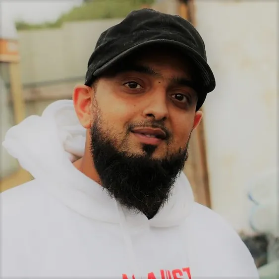a picture of a beared man in a white hoodie wearing a black hat, simling at the camera